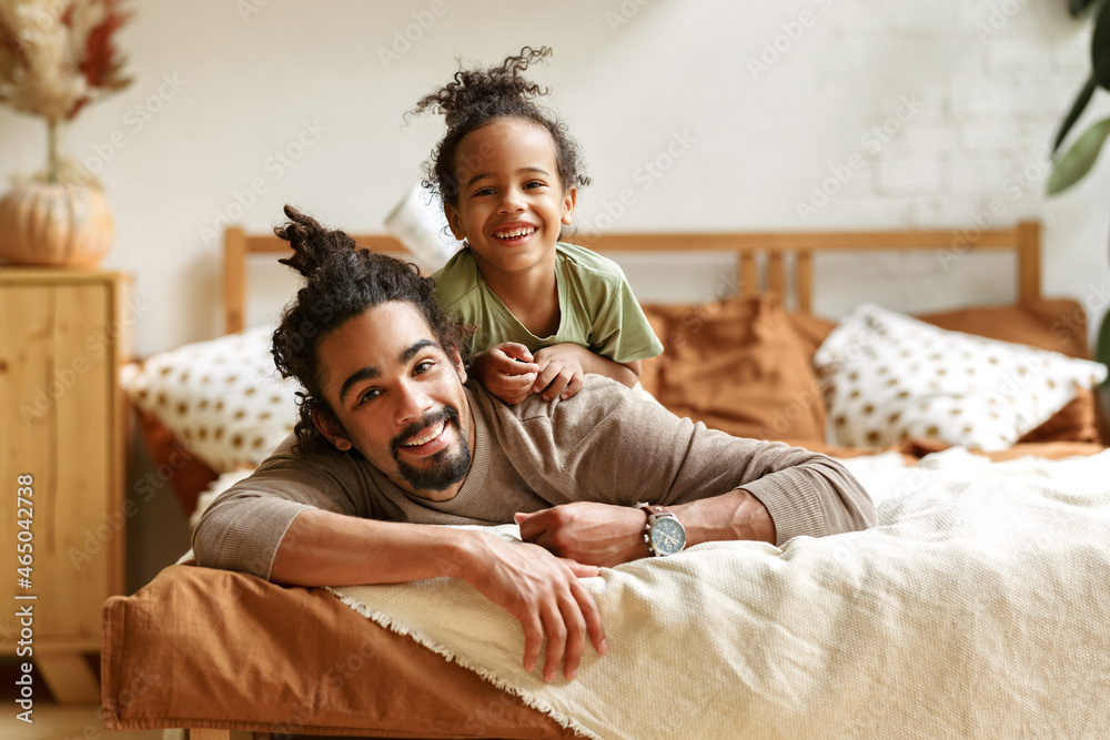 快乐的美国黑人家庭父亲和可爱的小儿子在家躺在床上放松