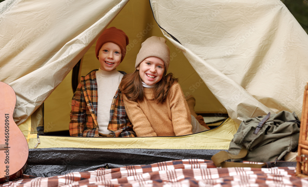 快乐的孩子们坐在旅游帐篷里，在露营旅行中对着镜头开心地微笑