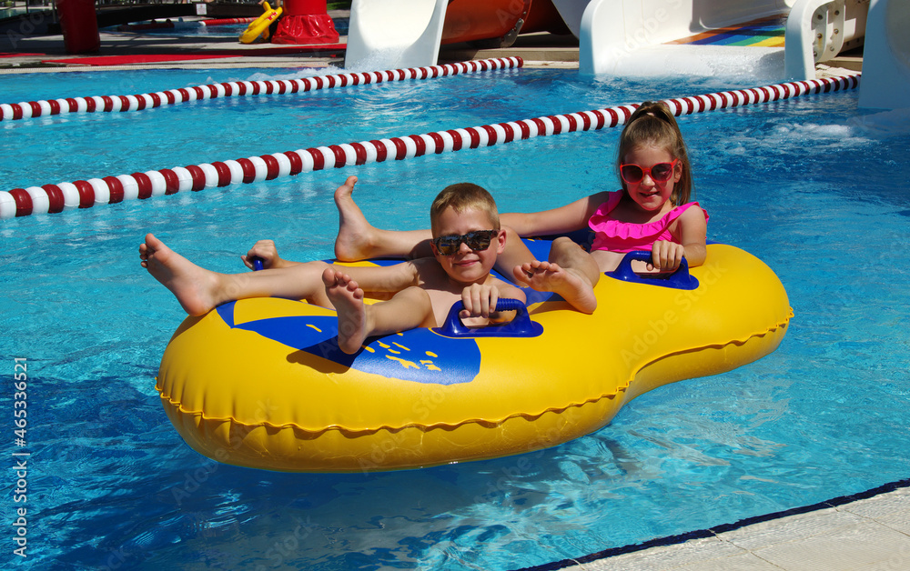室外游泳池里，男孩和女孩在充气浮漂上。