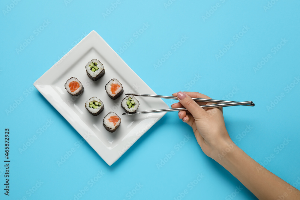 女人在彩色背景上从盘子里取出美味的寿司卷