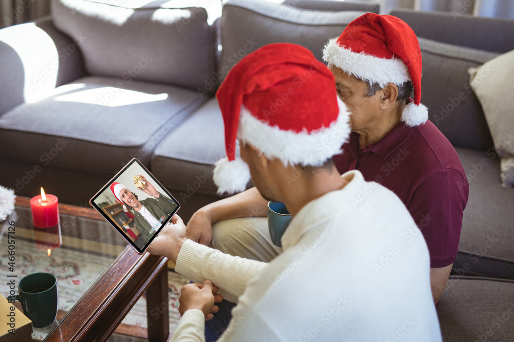 戴着圣诞老人帽的混血父亲和成年儿子与男性朋友进行平板电脑圣诞视频通话
