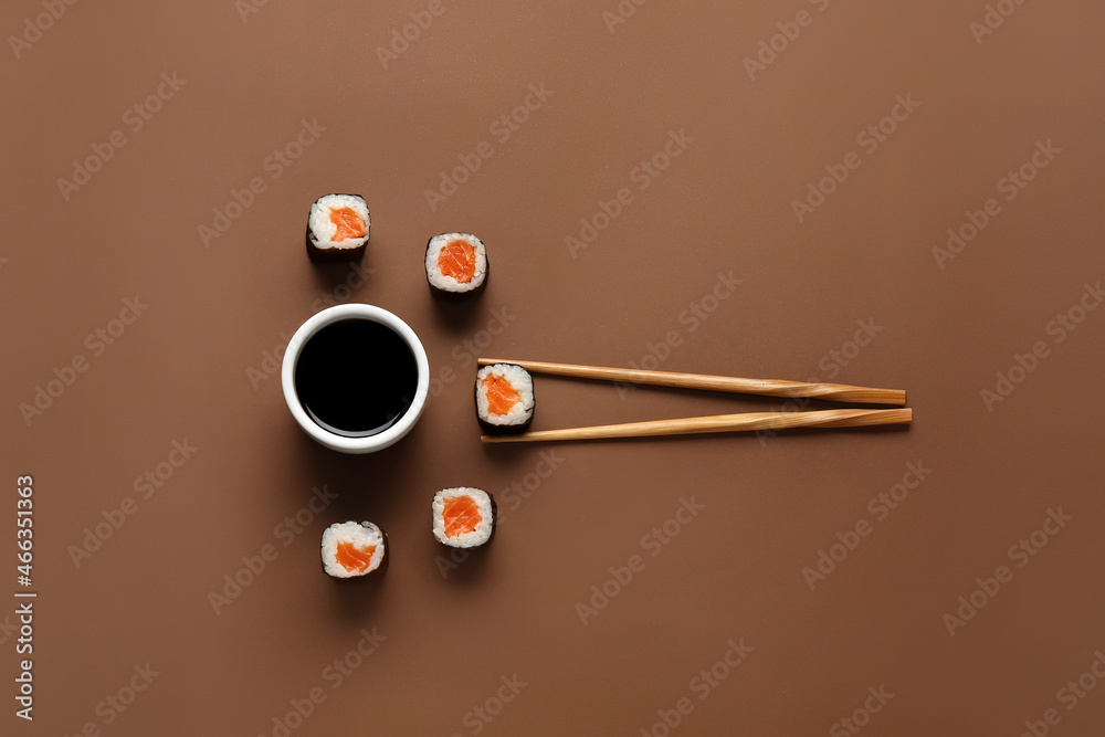 Salmon maki sushi, wooden chopsticks and bowl with soy sauce on color background