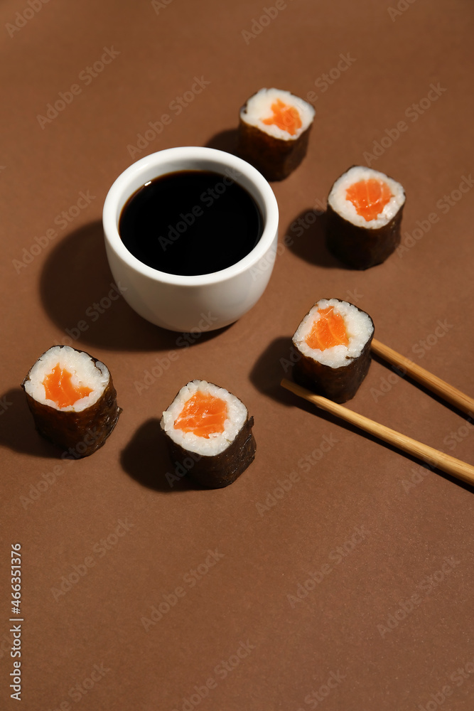 Salmon maki sushi, wooden chopsticks and bowl with soy sauce on color background, closeup