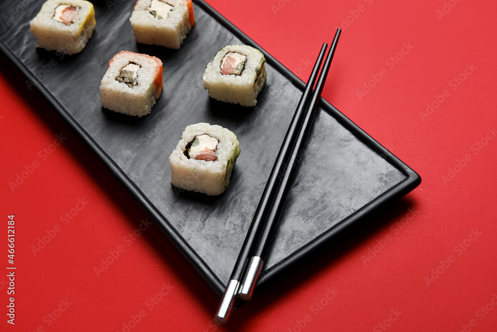 Tray with tasty sushi rolls and chopsticks on color background, closeup