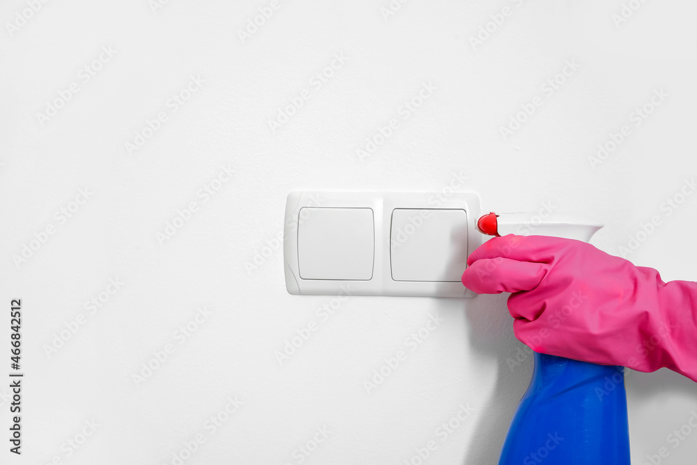 Woman spraying switch on white wall, closeup