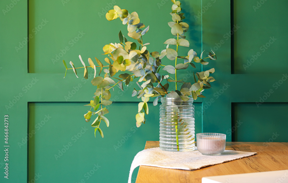 绿色墙壁附近桌子上有桉树树枝和蜡烛的花瓶
