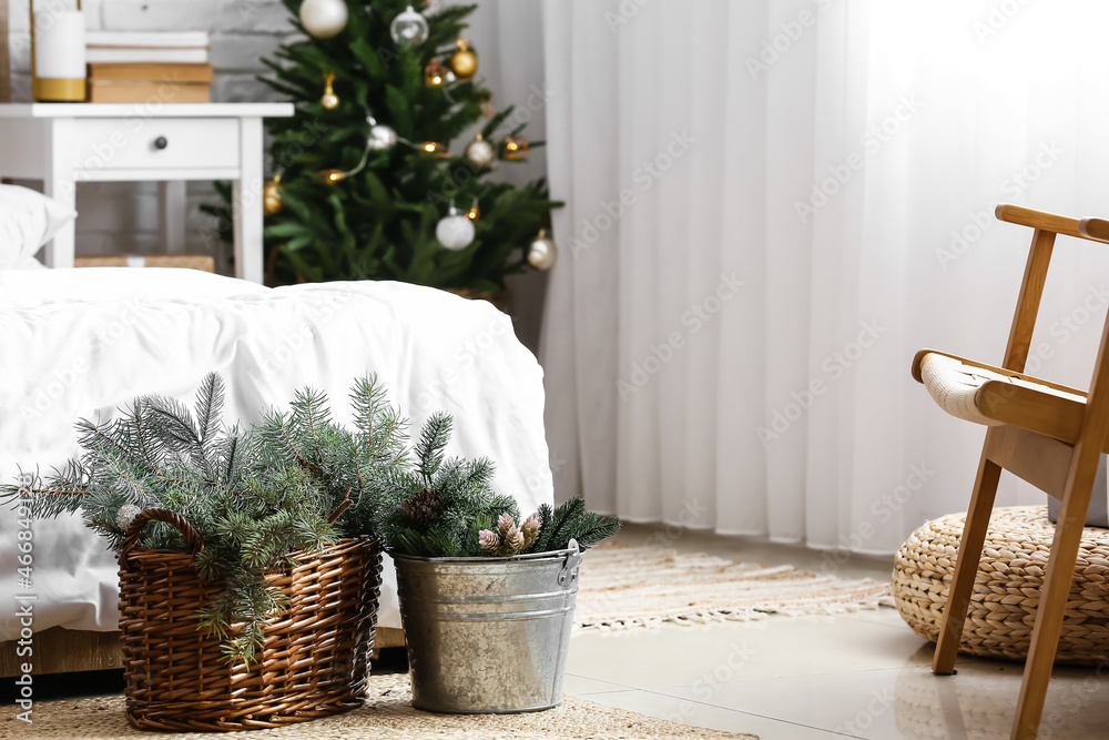 Basket and bucket with fir branches near bed in room