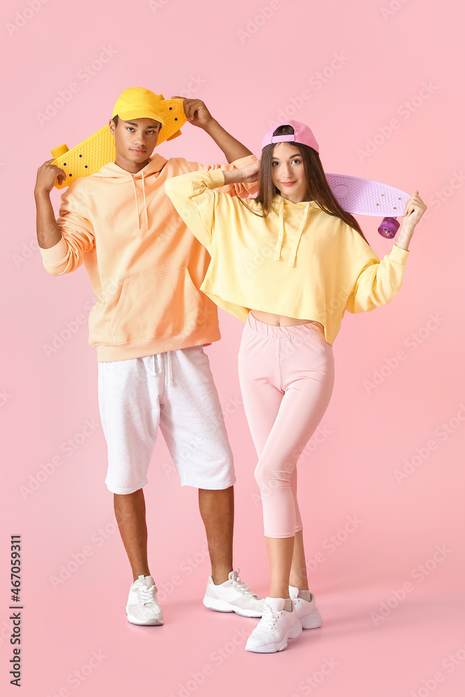 时尚的年轻滑冰情侣穿着粉色背景的连帽衫