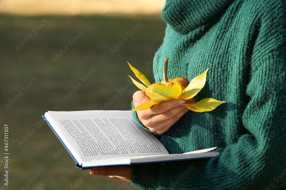 Woman with book and autumn leaf in park, closeup
