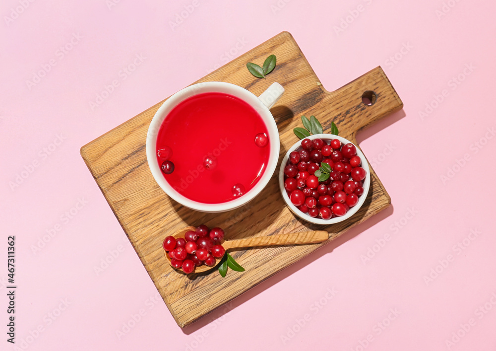 Wooden board with cup of tasty lingonberry tea and berries on color background