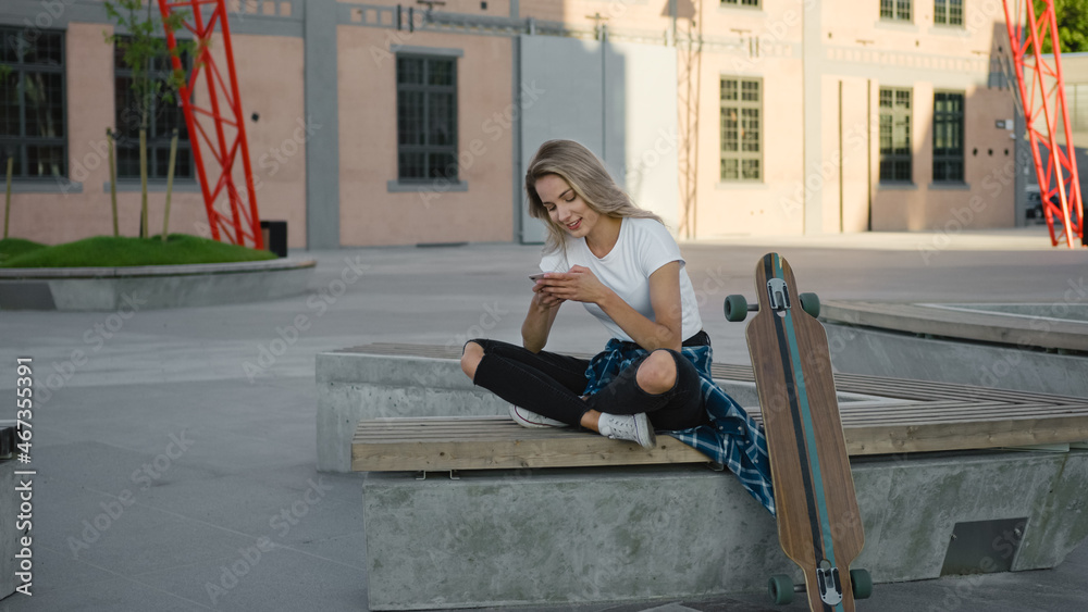 穿着休闲服、使用智能手机、在社交媒体上分享信息的漂亮金发滑冰女孩