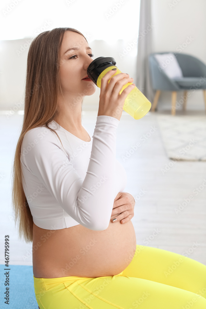 穿着时尚运动服的年轻孕妇在家喝水