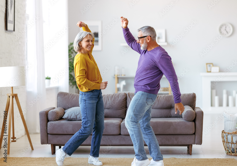 活力四射的高级家庭情侣在家里的客厅里一起跳舞，随着音乐翩翩起舞
