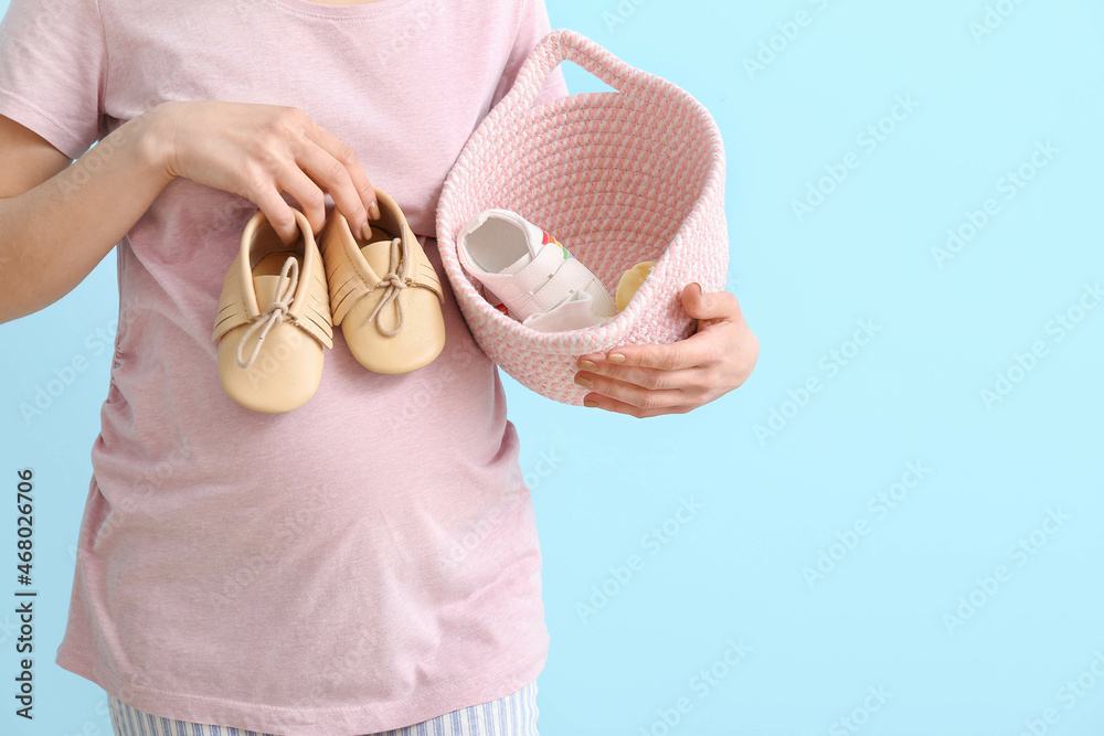 年轻孕妇拿着篮子，蓝色背景是婴儿鞋