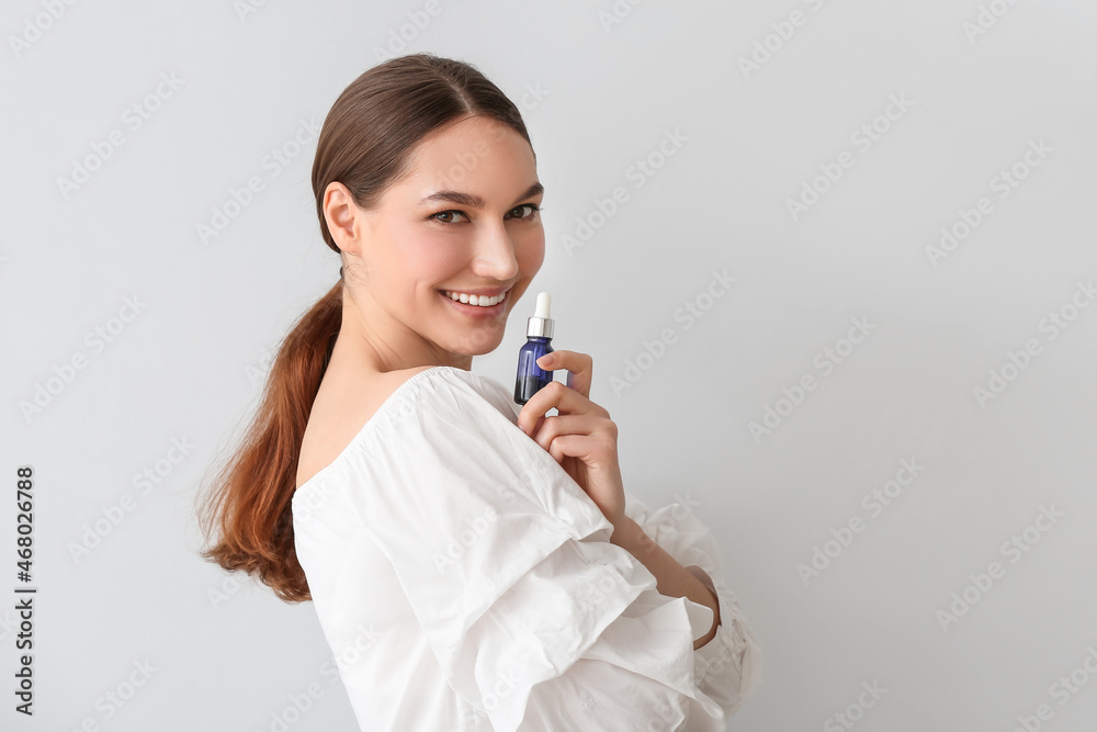 Portrait of smiling woman holding bottle of essential oil on light background