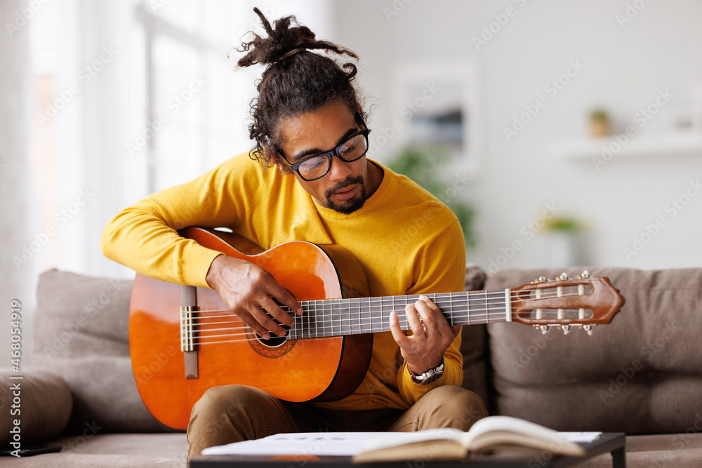 年轻快乐的非裔美国男子在家弹原声吉他，坐在客厅的沙发上