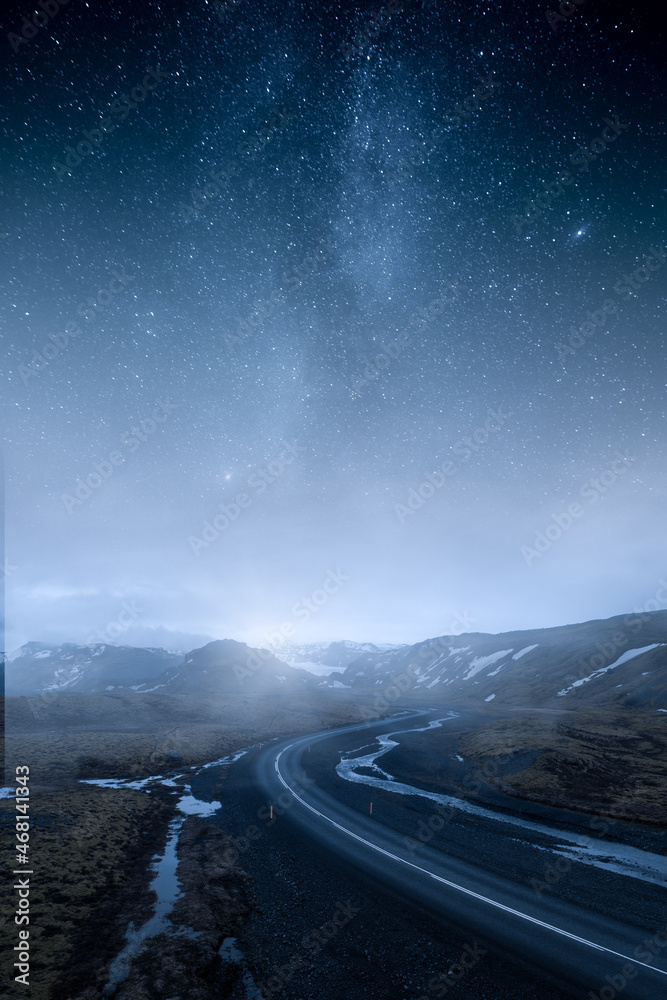 冰岛蜿蜒潮湿的道路通向群山，天空中有史诗般的星星和银河。