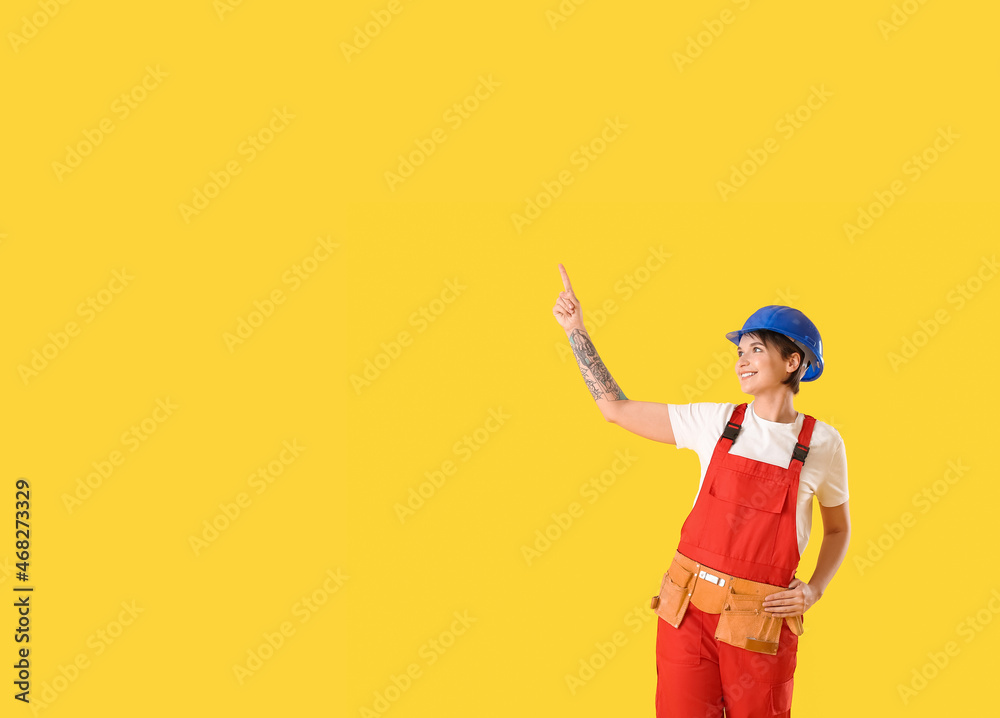 戴安全帽的女建筑工人指着黄色背景上的东西