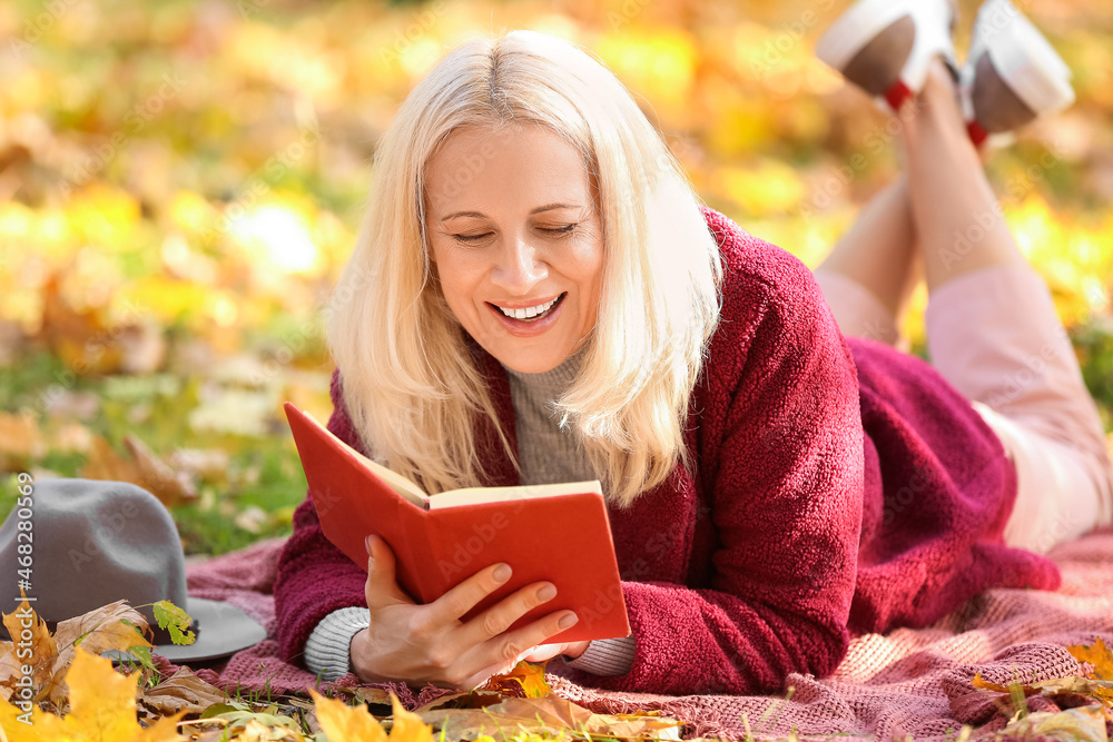 成熟女人在秋季公园看书