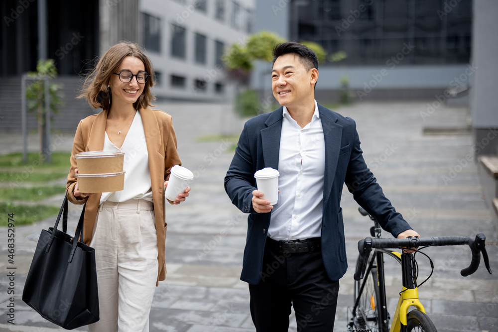 Asian businessman and caucasian businesswoman walking, drinking coffee and talking in city. Concept 