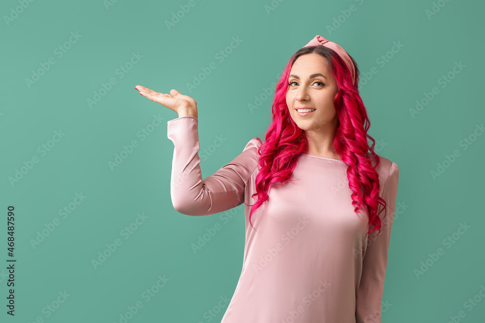 Beautiful woman with unusual bright hair showing something on color background