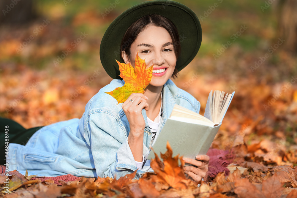 公园里挂着秋叶和书的微笑女人的肖像