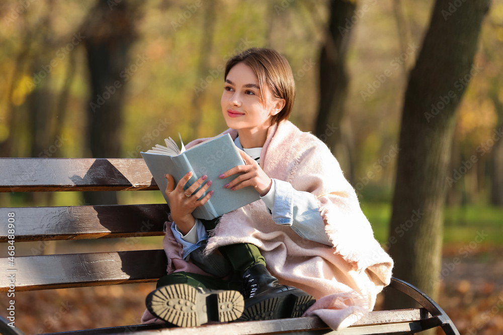 秋天公园木长椅上有格子和书的年轻女人