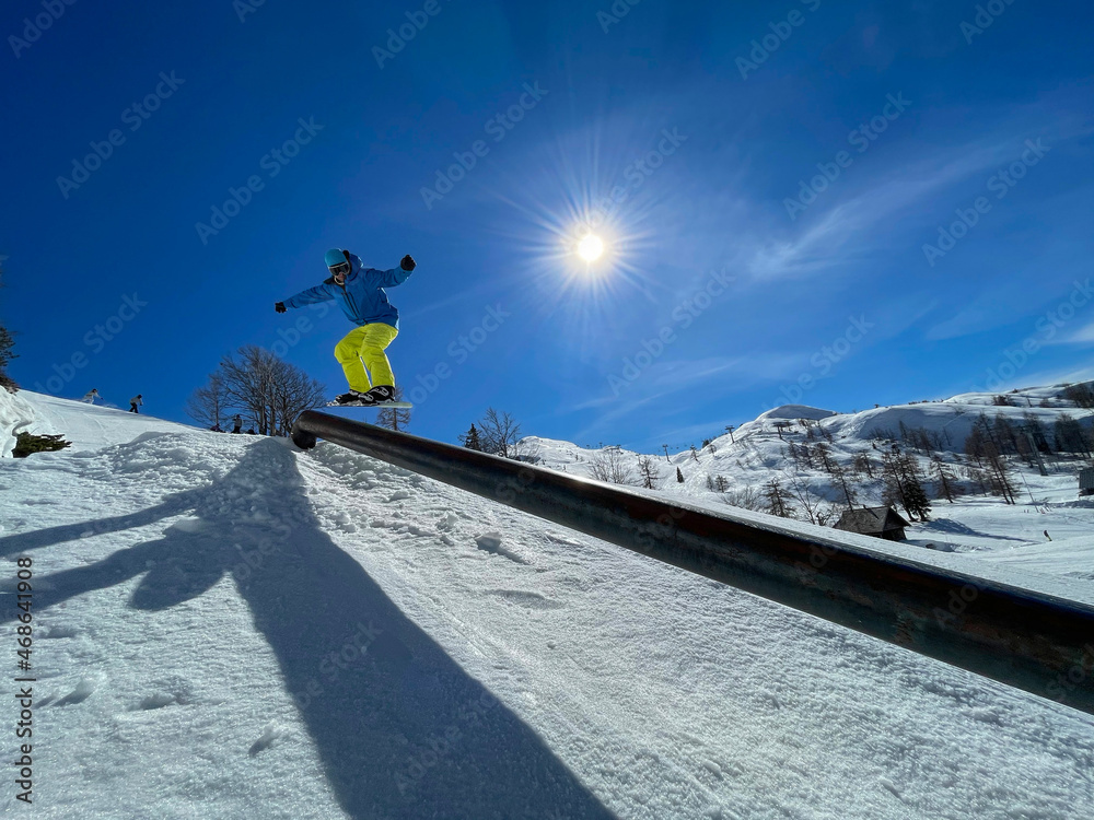 LENS FLARE: Athletic snowboarder does a railslide trick while riding in fun park