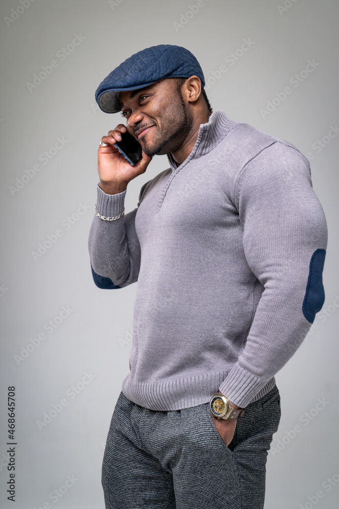 一名非洲男子半转身站在那里打手机。肌肉发达的男性穿着灰色休闲服