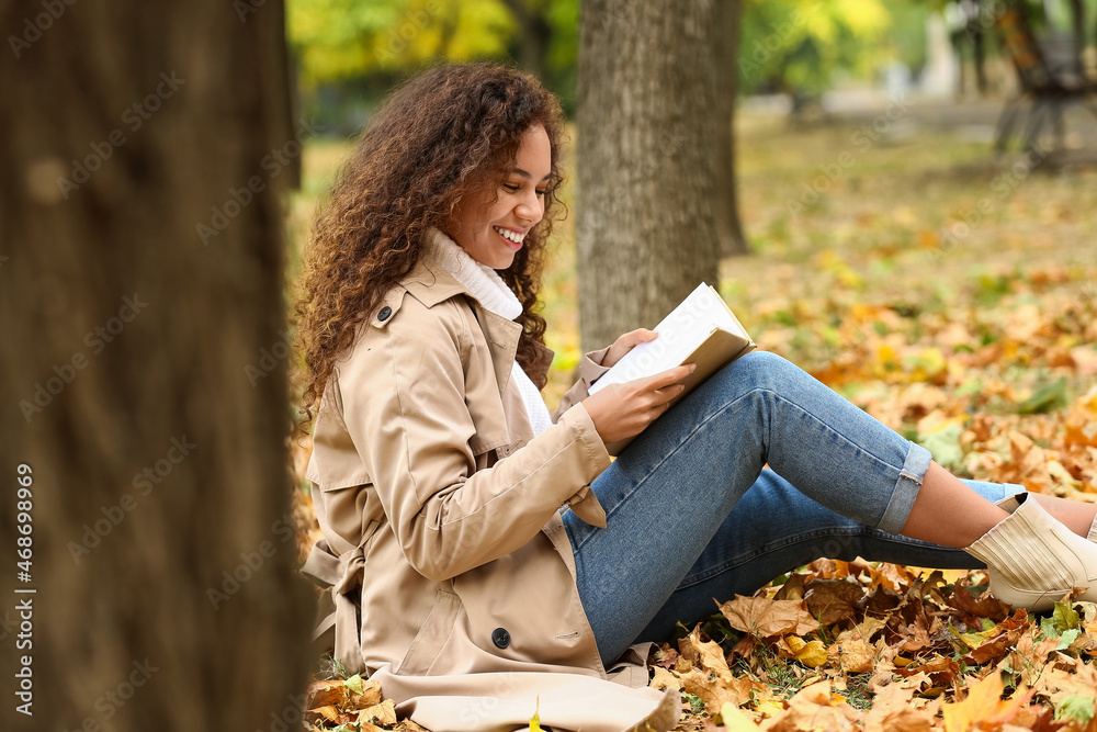 年轻微笑的非裔美国妇女在秋季公园看书
