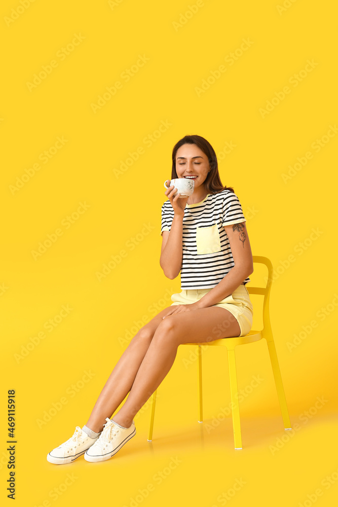 Beautiful woman with cup of coffee sitting on chair against color background