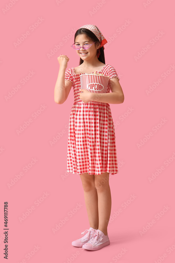 可爱的女孩，粉红色背景上有一桶爆米花