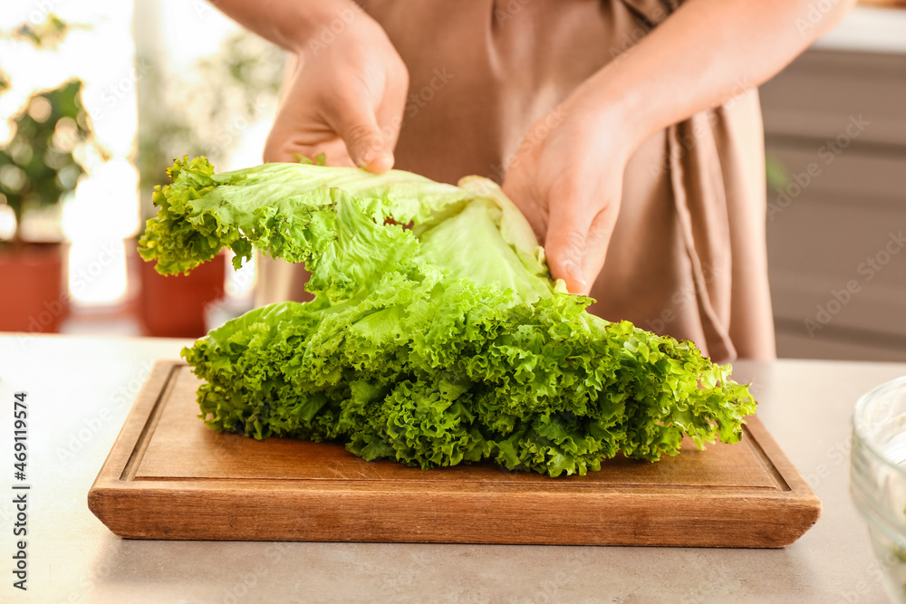 Woman with bunch of fresh lettuce in kitchen, closeup