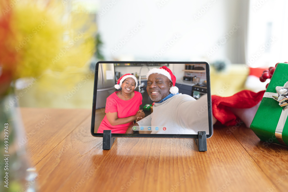 Happy senior african american couple in santa hats smiling on tablet video call screen at christmas