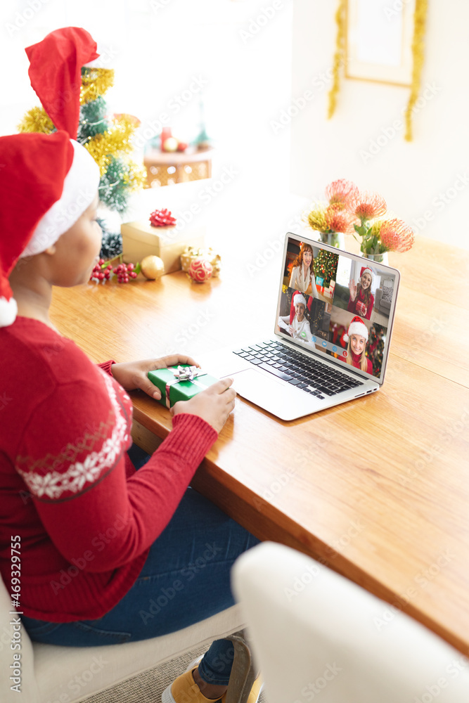 African american woman in santa hat making laptop christmas group video call with female friends