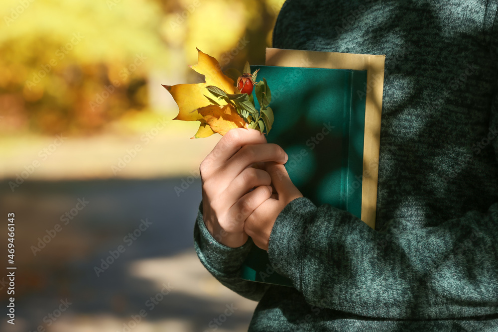 Woman holding book with autumn leaves in park, closeup
