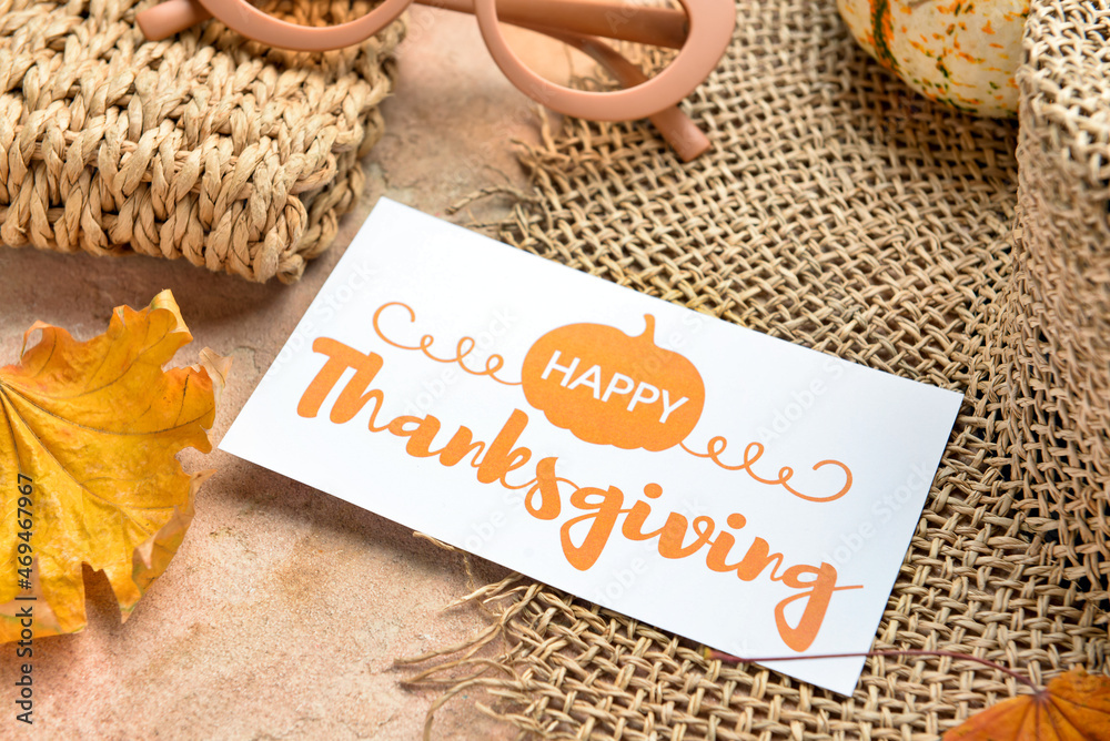 Wicker hat, dry leaves and paper card with text HAPPY THANKSGIVING on color background, closeup