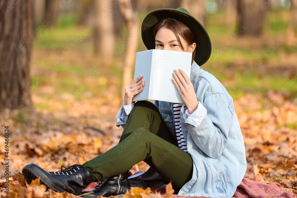 Pretty woman with book on plaid in autumn park
