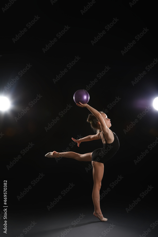 小女孩在黑暗背景下用球做体操