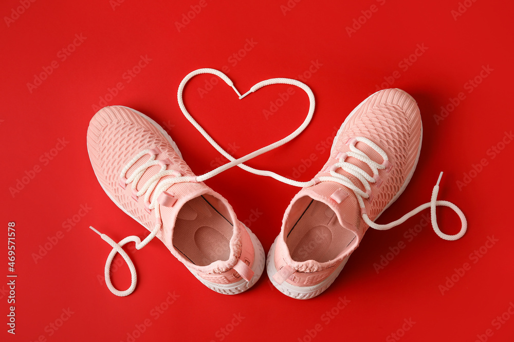 Pair of sportive shoes and heart made of laces on red background