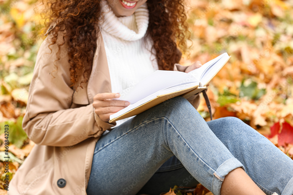 Attractive African-American woman reading book in autumn park, closeup