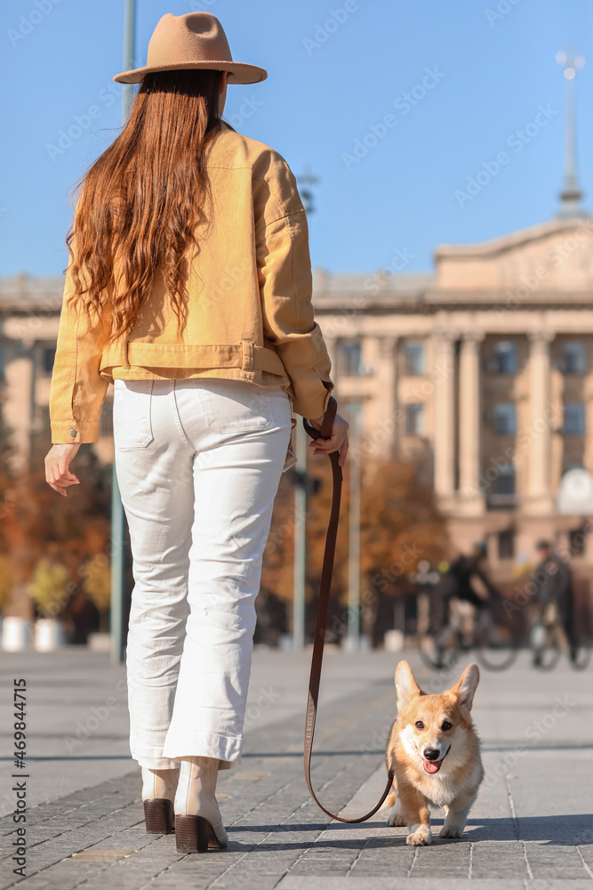 时尚年轻女子与可爱的柯基犬在城市广场散步
