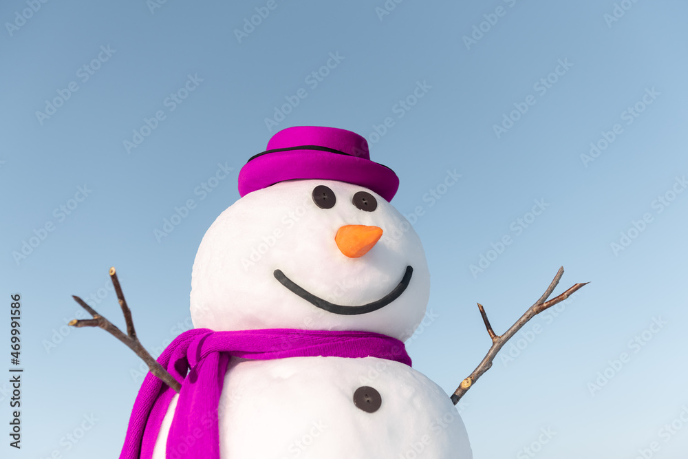雪地上戴着时髦的棕色帽子和粉色鳞片的有趣雪人。背景是蓝天