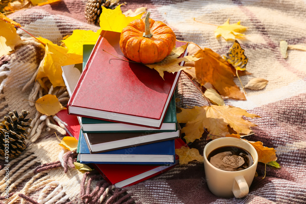 秋天公园里格子布上的一叠书、南瓜、一杯咖啡和树叶