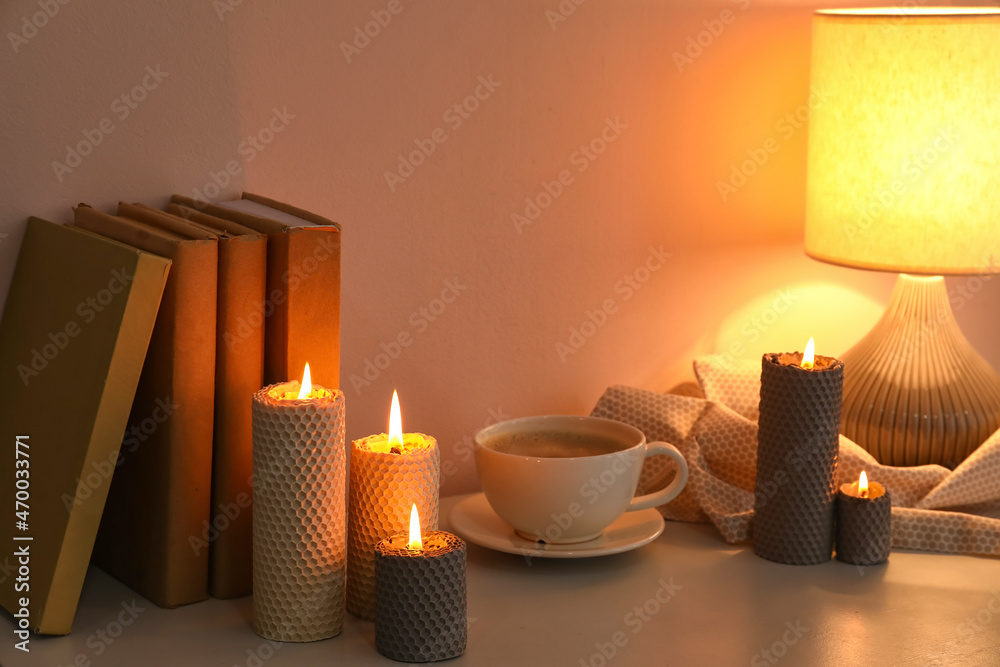 在靠近墙壁的桌子上燃烧蜡烛、一杯咖啡、书籍和发光的灯