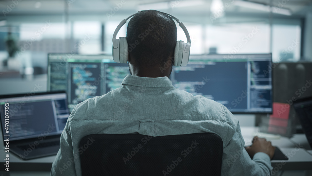 办公室：专业黑人IT程序员在台式电脑上工作时使用耳机。男性网站
