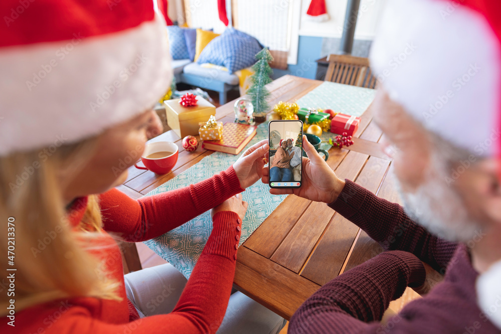 Caucasian couple in santa hats making smartphone christmas video call with diverse senior friends
