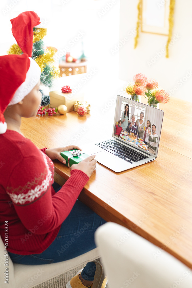戴着圣诞帽的非洲裔美国妇女与微笑的白人家庭进行笔记本电脑圣诞视频通话
