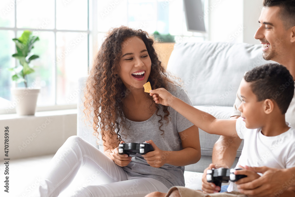 快乐的跨种族家庭在家玩电子游戏和吃薯片