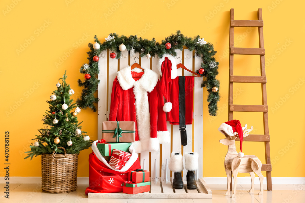 Hanger with Santa Claus costume, boots, bag with presents, Christmas tree and ladder near color wall